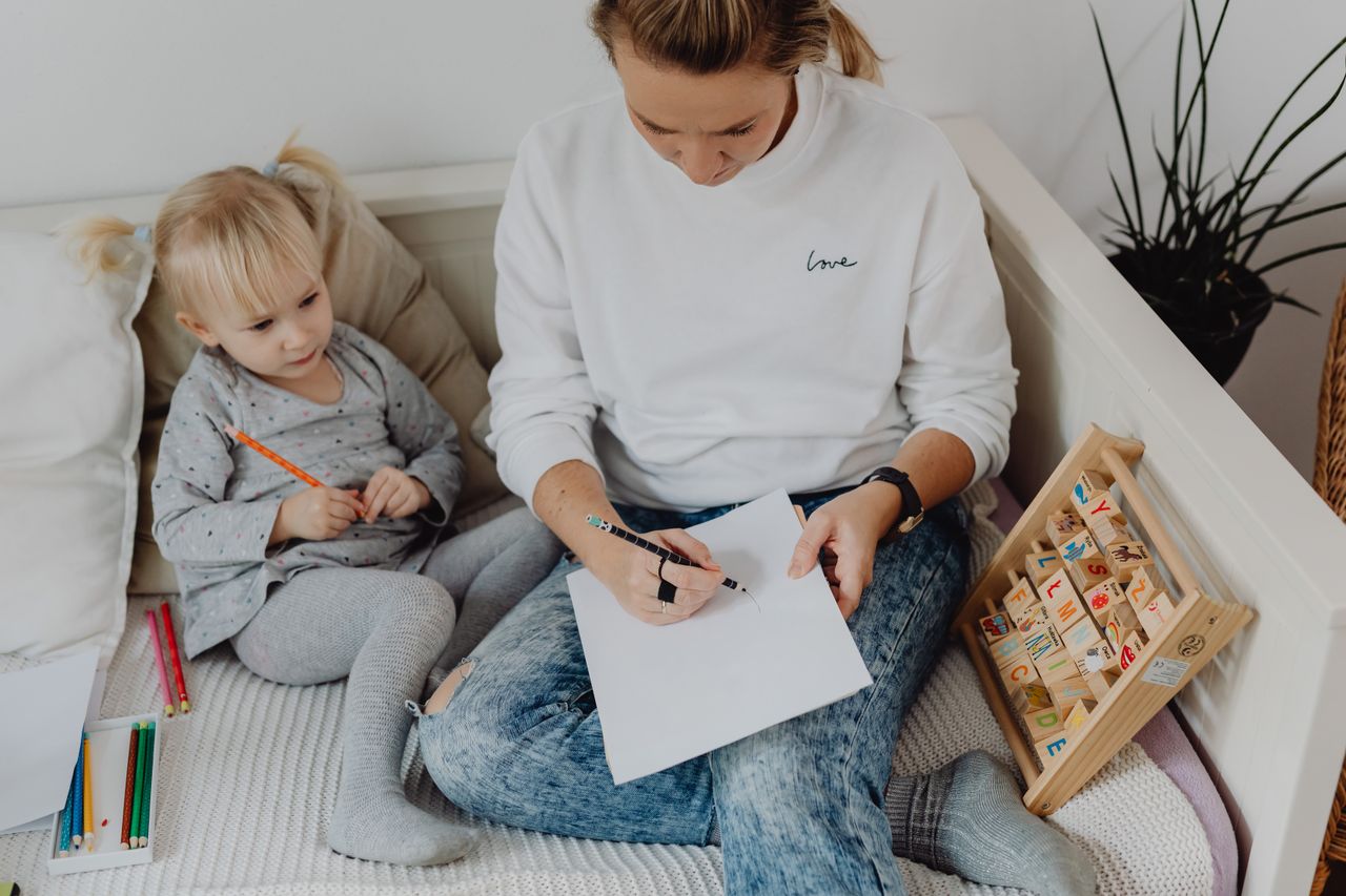 A mother guides her child in learning with colorful pencils and alphabet blocks.
